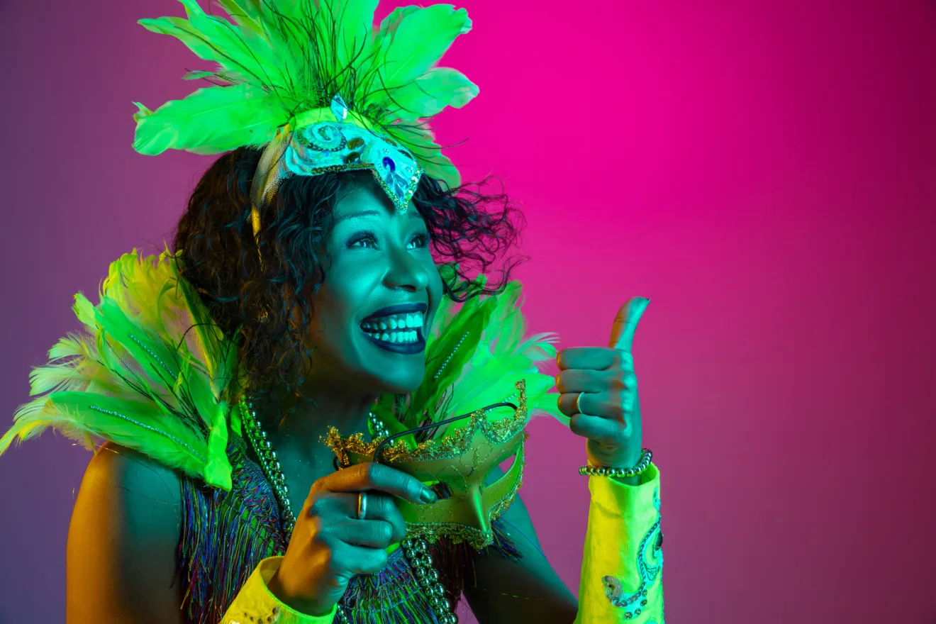 Laughting. Beautiful young woman in carnival, stylish masquerade costume with feathers dancing on gradient background in neon. Concept of holidays celebration, festive time, dance, party, having fun.